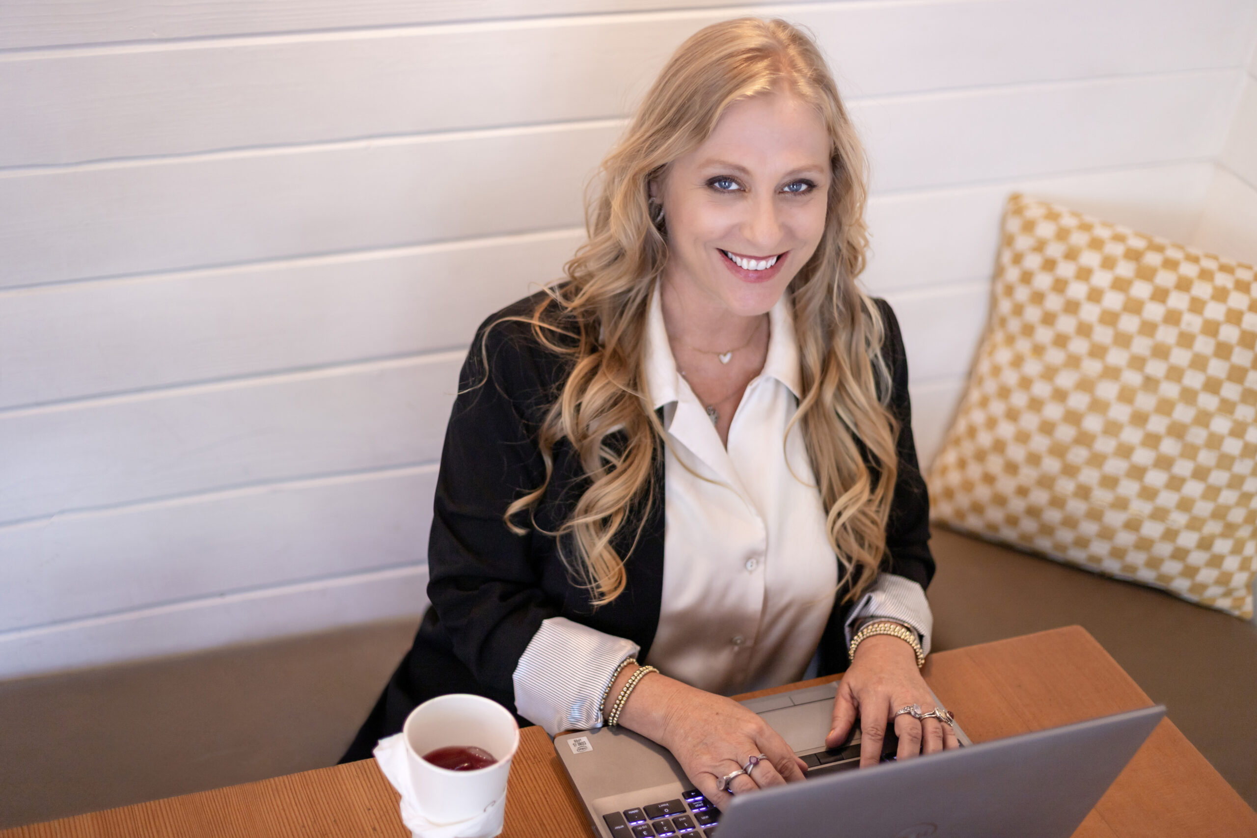 Julianne, a dedicated Medicare Insurance Advocate, smiles while working on her laptop at a cozy café table — helping clients navigate their Medicare options with care and expertise.